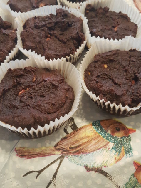 Nahaufnahme von Schokoladen-Muffins in Papierförmchen auf einem Stoff mit Vogelmuster, warme und gemütliche Atmosphäre